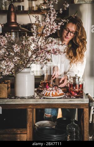 Donna taglio casalinga senza glutine torta di bundt vicino rami fioritura Foto Stock