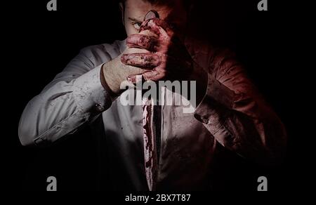 Foto horror di un assetato di sangue assalito che posa con il grande coltello da cucina sanguinoso che tiene in entrambe le mani. Foto Stock