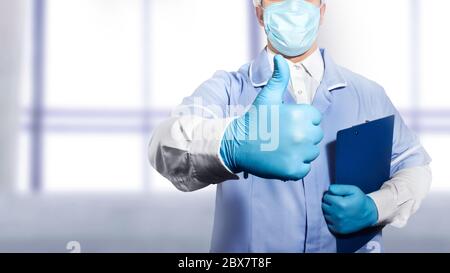 Foto di un medico in completo vestito e guanti di gomma che tengono una tavoletta per i documenti e mostrando pollici in su. Foto Stock