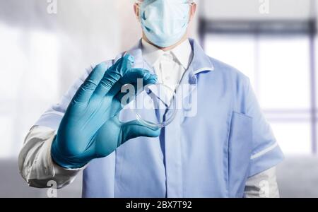 Foto di un assistente di laboratorio che tiene una tazza di Petri in un abito a corpo pieno e guanti di gomma. Foto Stock