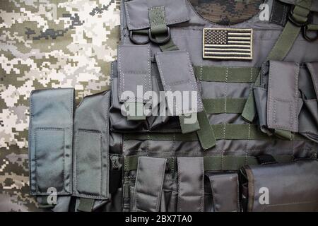 Foto dall'alto di un gilet militare tattico antiproiettile con stemma americano posto sullo sfondo di un panno camouflage. Foto Stock