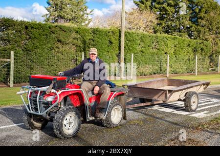 Annat, Canterbury, Nuova Zelanda, maggio 26 2020: Un agricoltore in pensione tira un rimorchio dietro la sua moto quad per raccogliere le decorazioni di siepi su una strada rurale Foto Stock