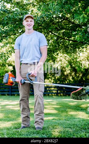 giovane uomo sorridente che indossa cappello che tiene mangiatore di erbacce Foto Stock