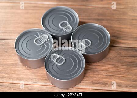 quattro lattine di tonno color argento su tavolo di legno marrone, vista dall'alto Foto Stock