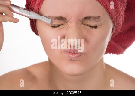 Giovane bella ragazza in un asciugamano rosso la cura per le sopracciglia con trimmer Foto Stock