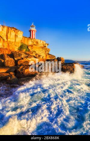 Faro Hornby bianco-rosso all'ingresso del porto di Sydney dall'oceano Pacifico in morbida luce mattutina contro il cielo blu chiaro. Foto Stock