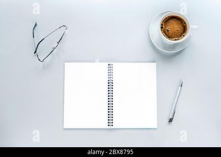 Tazza di caffè e mockup a spirale vuoto del blocco note su uno sfondo grigio con penna e occhiali. Concetto di lavoro da casa. Vista dall'alto, disposizione piatta Foto Stock