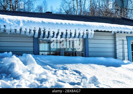 Bella foto di neve e ricicli piegati appesi al tetto della tradizionale cabina svedese in legno azzurro sulle montagne di Lappand, Svezia settentrionale. Foto Stock
