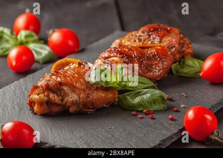 Cosce di pollo e basilico in una padella nera in ghisa su un tavolo di legno Foto Stock