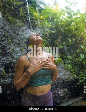 vacanze avventura ritratto stile di vita - giovane bella e felice donna prendendo doccia naturale dalla cascata nella giungla godendo la natura spensierata Foto Stock