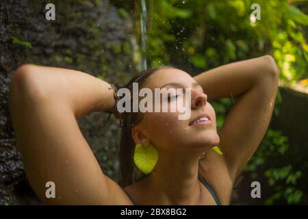 vacanze avventura ritratto stile di vita - giovane bella e felice donna prendendo doccia naturale dalla cascata nella giungla godendo la natura spensierata Foto Stock