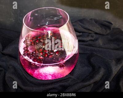 Un melograno rosso, Gin e tonico, guarnito con una grande quantità di poits di melograno, su sfondo nero Foto Stock