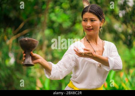 Connessione mente e corpo - bella e felice guaritrice donna asiatica tenendo incenso tazza facendo rituale tradizionale danza guarigione a verde foresta tropicale Foto Stock