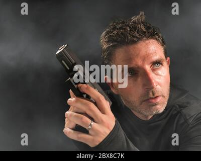 ritratto d'azione di un serio e attraente hitman o agente speciale uomo che tiene la pistola puntando la pistola a sfondo cinematografico edgy in servizio segreto Foto Stock