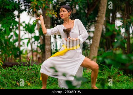 Connessione mente e corpo - bella e felice guaritrice donna asiatica tenendo incenso tazza facendo rituale tradizionale danza guarigione a verde foresta tropicale Foto Stock