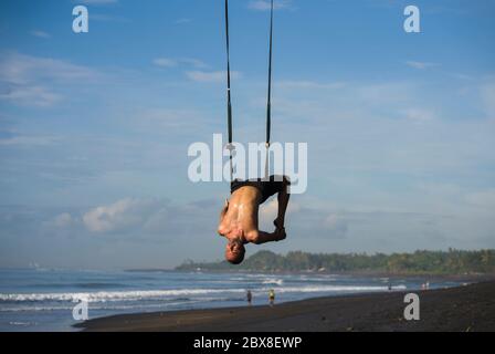 all'aperto ritratto di uomo che pratica aero yoga allenamento in spiaggia appeso da altalena corda sopra il mare allenamento equilibrio corpo e flessibilità in hea Foto Stock