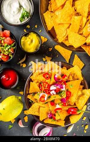 Nachos chips con formaggio fuso e varie salse messicane tradizionali, salsa e jalapeno, sfondo grigio scuro spazio copia vista dall'alto Foto Stock