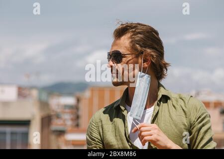 Bell'uomo europeo di mezza età in occhiali da sole che toglieva la maschera al sole. Non più quarantena. Coronavirus è finito, concetto di libertà. Foto Stock