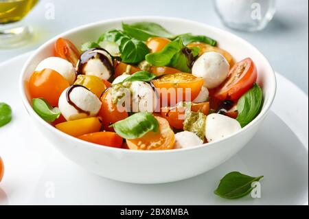 Insalata caprese con pomodori e polpette di mozzarella in ciotola bianca. Mozzarella di bocconcini con foglie di basilico. Foto Stock