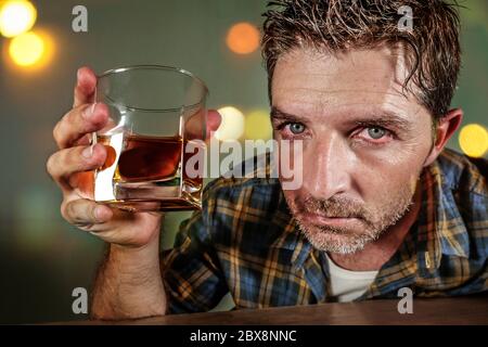 giovane alcolista triste e depresso con bicchiere di whisky sprecato e ubriaco non resistendo a bere in bar pub di notte cadere in abuso di alcol Foto Stock