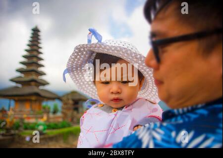 Giovane felice e orgoglioso cinese asiatico come padre amorevole che tiene adorabile figlia bambina durante le vacanze escursione visitando il tempio di Bali in famiglia Foto Stock