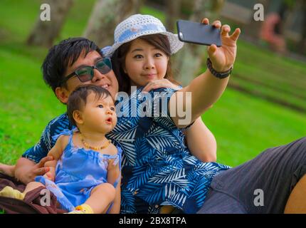 Giovane felice e amorevole famiglia asiatica coreana con genitori e dolce figlia bambino al parco della città insieme con il padre che prende foto selfie con il telefono cellulare Foto Stock