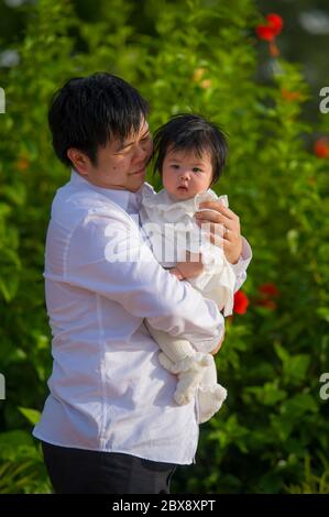 giovane uomo felice e orgoglioso come padre di bambina dolce che tiene la figlia di fronte al giardino dei fiori al resort vacanze godendo insieme Foto Stock