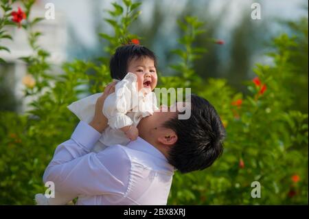 giovane uomo felice e orgoglioso come padre di bambina dolce che tiene la figlia di fronte al giardino dei fiori al resort vacanze godendo insieme Foto Stock