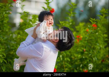 giovane uomo felice e orgoglioso come padre di bambina dolce che tiene la figlia di fronte al giardino dei fiori al resort vacanze godendo insieme Foto Stock