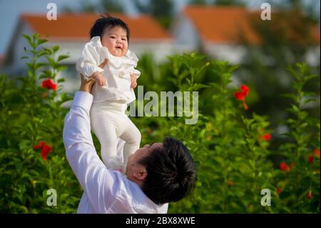 giovane uomo felice e orgoglioso come padre di bambina dolce che tiene la figlia di fronte al giardino dei fiori al resort vacanze godendo insieme Foto Stock