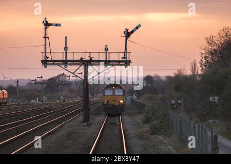 DB CARGO UK classe 66 locomotiva 66160 che si avvicina al semaforo della staffa a Barnetby con un treno merci al crepuscolo Foto Stock