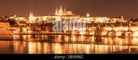 Praga d'oro di notte. Il Castello di Praga e il Ponte Carlo si riflettono nel fiume Moldava. Vista dall'argine Smetana. Praha, Repubblica Ceca. Foto Stock