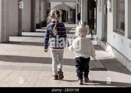 Due bambini camminano insieme a mano nella vecchia strada porticata della città. Amore di famiglia e tema di amicizia. Foto Stock