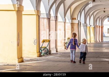 Due bambini camminano insieme a mano nella vecchia strada porticata della città. Amore di famiglia e tema di amicizia. Foto Stock