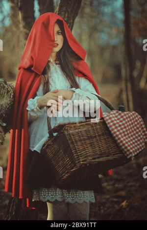 Ritratto scuro di cappuccio rosso piccolo con cesto di vimini nella foresta Foto Stock