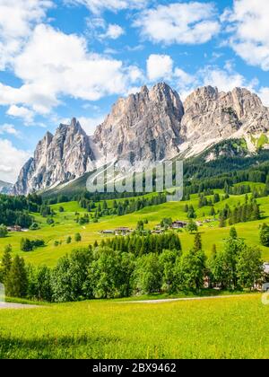 Crinale roccioso del Monte Pomagnon sopra Cortina d'Ampezzo con prati verdi e cielo blu con bianche nuvole estive, Dolomiti, Italia. Foto Stock