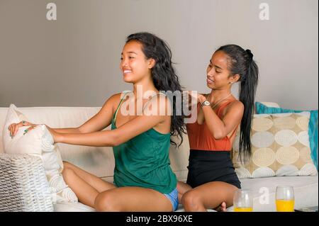 Giovane bella e felice girlfriends asiatica a casa divano con una ragazza che spazzolava i capelli dell'altra donna aiutando a preparare per datare chee sorridente Foto Stock