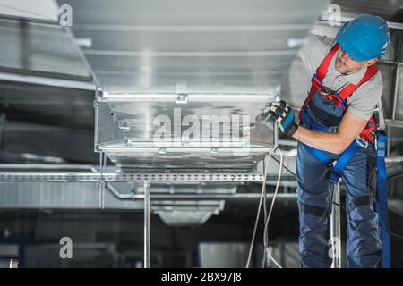 Tema industriale. Installazione dell'impianto di riscaldamento e raffreddamento del magazzino da parte di un tecnico caucasico professionista. Rettangolo ventilazione edifici commerciali CA Foto Stock