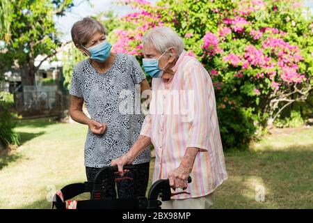 Caregiviere che aiuta la signora anziana ad allenarsi in giardino indossando la maschera Foto Stock