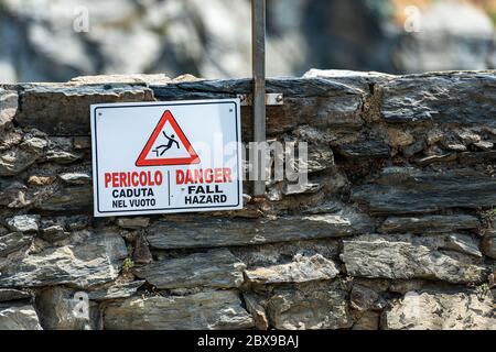 Cartello di avvertimento con il testo pericolo di caduta in inglese e italiano (Pericolo caduta nel vuoto) su una parete che si affaccia sulla scogliera del mare. Vernazza. Foto Stock