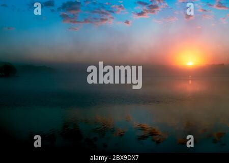 dawn sul lago sopra l'acqua e un pescatore solista su una barca Foto Stock