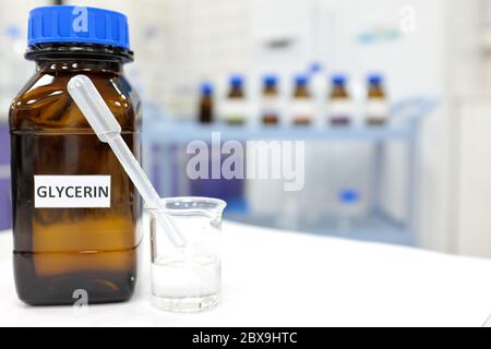 Bicchiere in vetro di glicerina e flacone color ambra marrone all'interno del laboratorio con spazio per la copia. Foto Stock