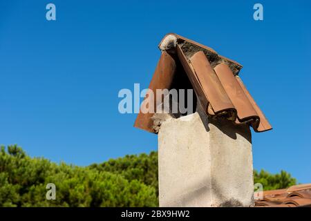 Primo piano di un camino di una casa con tetto in cotto su un cielo azzurro chiaro. Italia, Europa Foto Stock