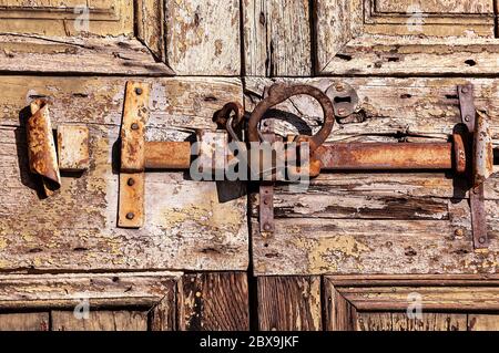 Primo piano di una vecchia porta in legno con un grande chiavistello in ferro arrugginito, lucchetto e tombino - Lombardia, Italia, Europa Foto Stock