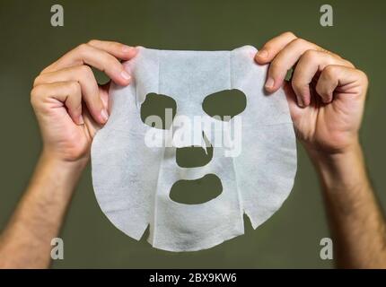 mani dell'uomo che tengono la maschera facciale di carta di bellezza isolata su sfondo uniforme nel concetto di cura della pelle del viso Foto Stock