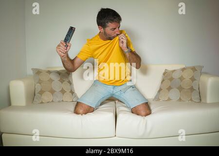 giovane eccitato e pazzo felice sostenitore di calcio uomo che guarda la partita di calcio in televisione sul divano del soggiorno che celebra la squadra che segna obiettivo feeling inte Foto Stock