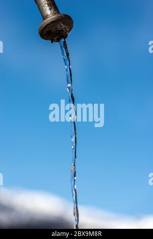 Estrema vicinanza di acqua fresca che scorre da un rubinetto all'aperto su un cielo azzurro in montagna (Alpi Italiane), Italia, Europa Foto Stock