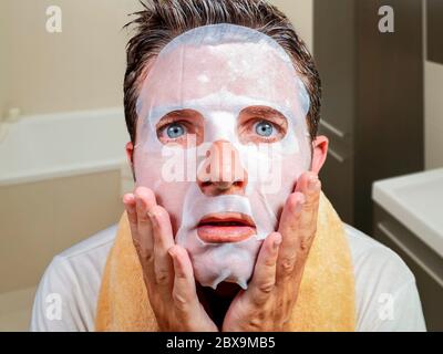 stile di vita bagno ritratto di giovane strano e divertente uomo a casa cercando di utilizzare carta di bellezza maschera facciale pulizia imparare anti invecchiamento trattamento in surp Foto Stock