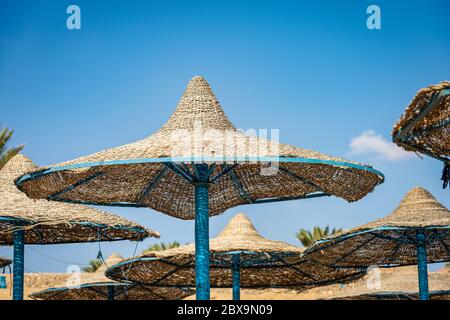 Gruppo di ombrelloni da spiaggia di paglia su cielo azzurro. Mar Rosso, Marsa Alam, Egitto, Africa. Foto Stock