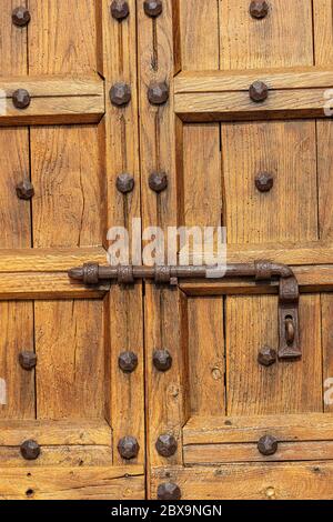 Primo piano di una vecchia porta di legno marrone con un grande chiavistello in ferro battuto e borchie. Provincia di Verona, Veneto, Italia, Europa Foto Stock